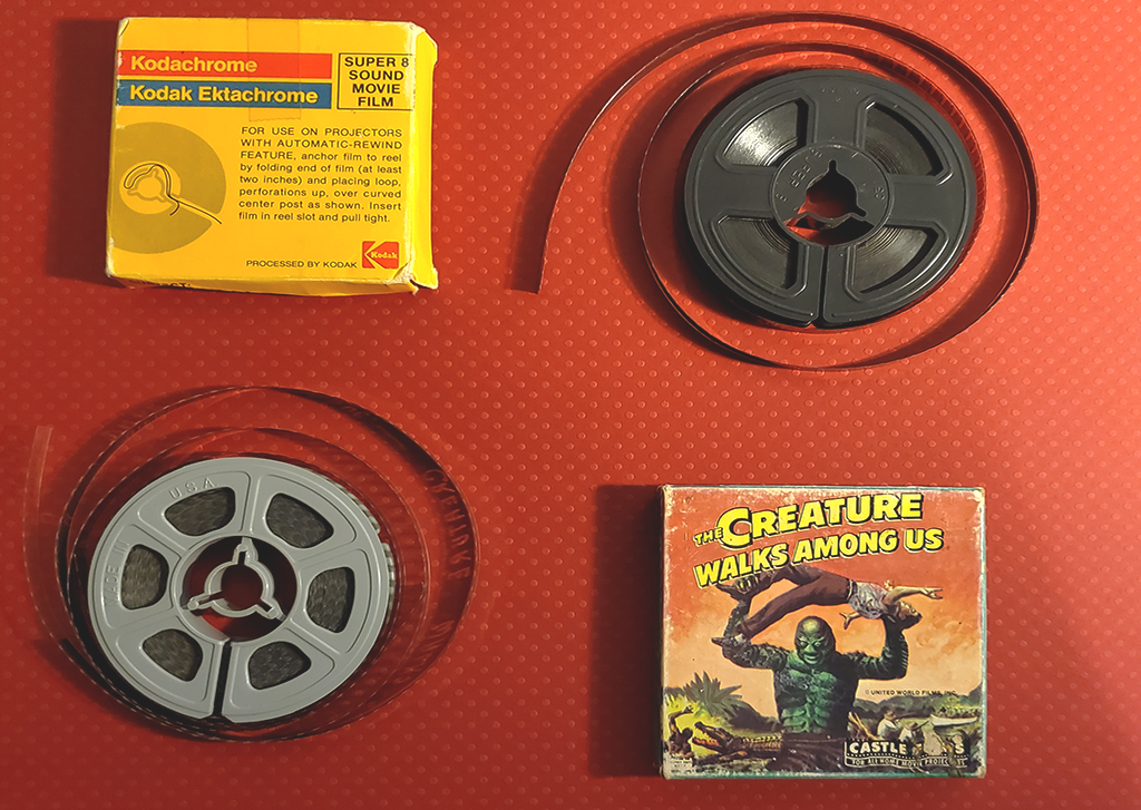 A photo of two 8mm film reels and two 8mm reel boxes on a red backround